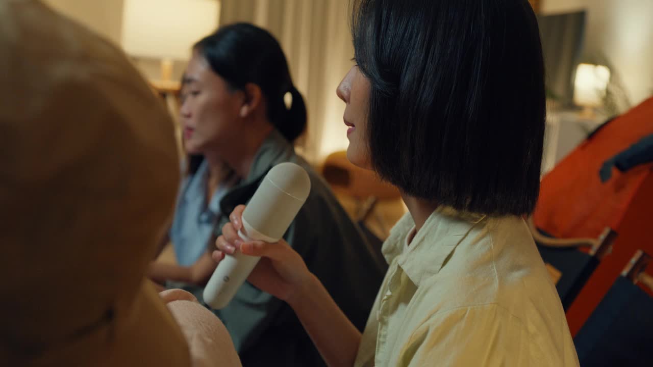 一群亚洲女性朋友晚上在家里的客厅里露营，一边唱歌一边用手机自拍视频通话。快乐的女人谈笑风生，享受休闲活动。视频下载