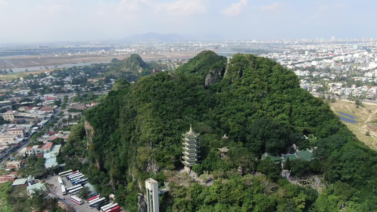 在一个阳光明媚的日子里，越南岘港市的无人机鸟瞰图，上面有满是树木的大理石山，周围是平坦的土地，周围是佛教寺庙视频素材