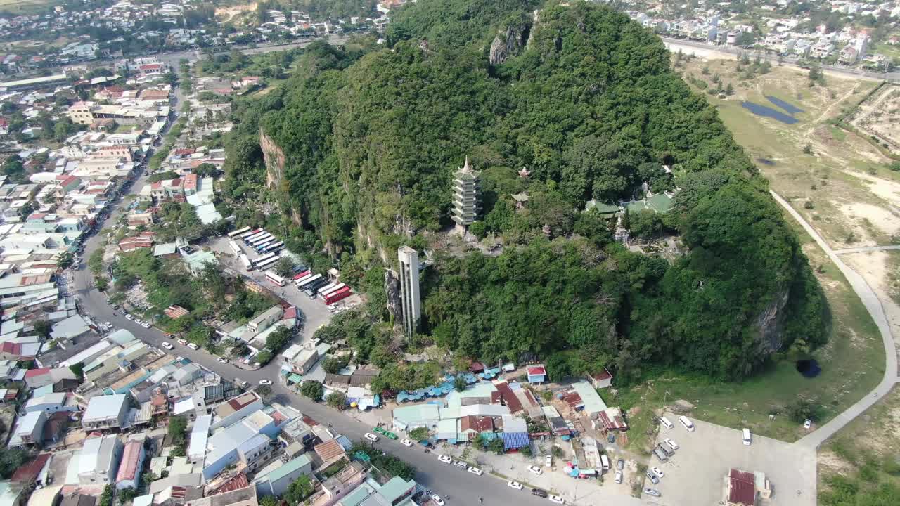 在一个阳光明媚的日子里，越南岘港市的无人机鸟瞰图，上面有满是树木的大理石山，周围是平坦的土地，周围是佛教寺庙视频素材