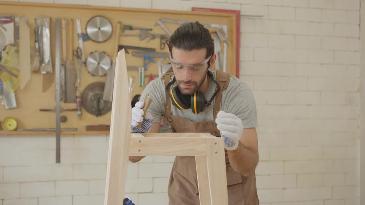 家具作坊的小企业主用笔记本电脑检查新木椅的图纸设计，帅气的木匠开始组装木椅视频下载