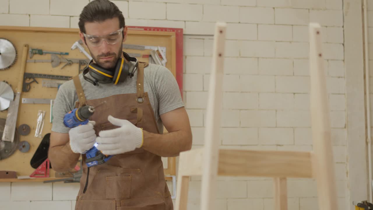 家具作坊的小企业主用笔记本电脑检查新木椅的图纸设计，帅气的木匠开始组装木椅视频下载