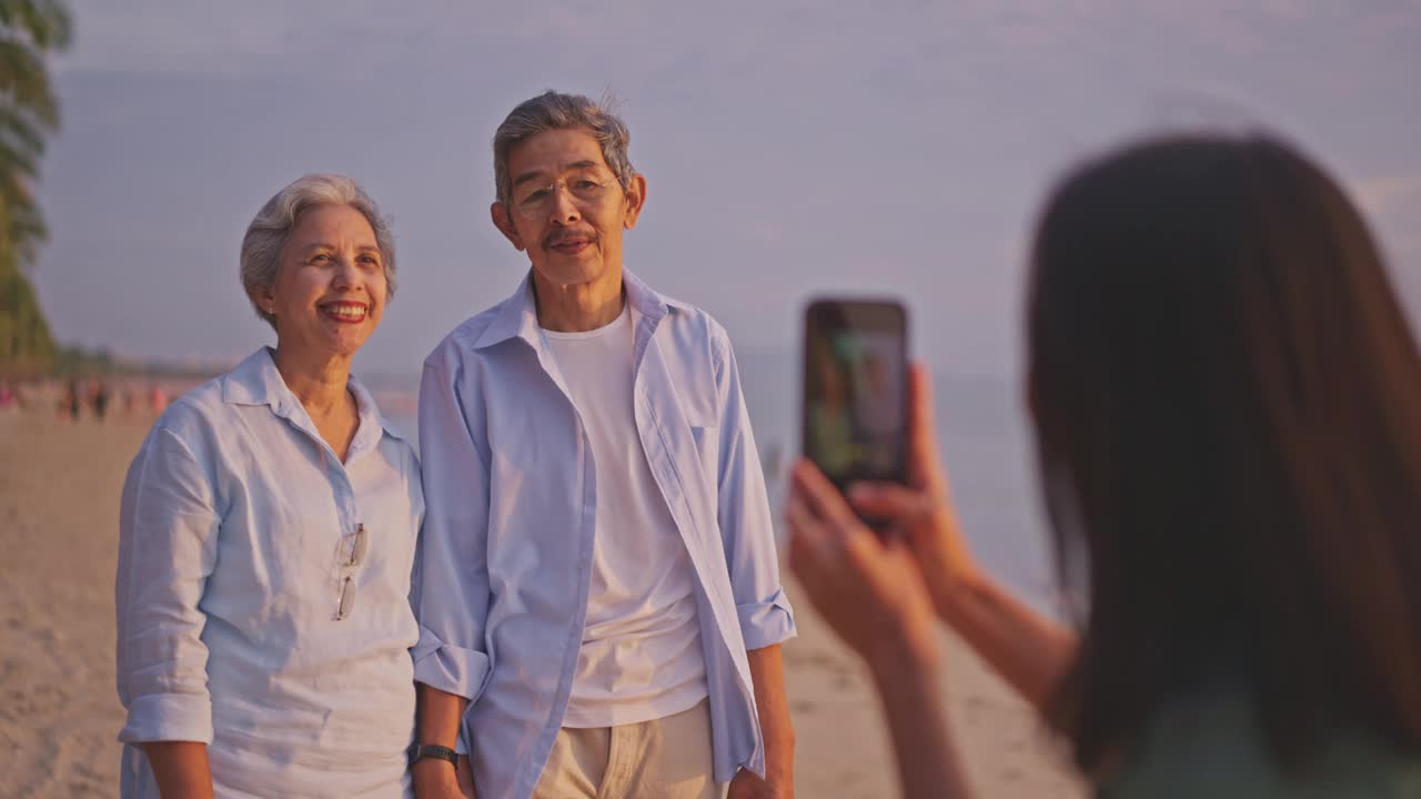 老夫妇一家在海滩上与当地导游一起享受，而她用智能手机拍照。视频下载