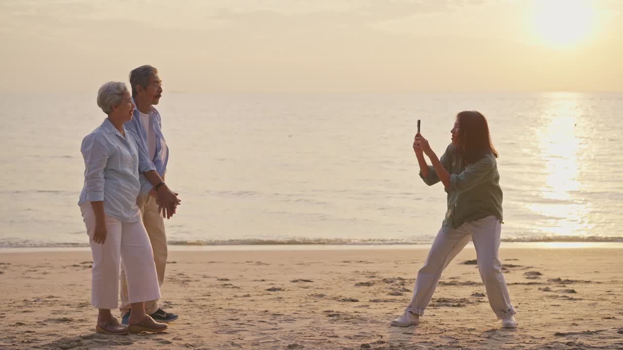 老夫妇一家在海滩上与当地导游一起享受，而她用智能手机拍照。视频下载