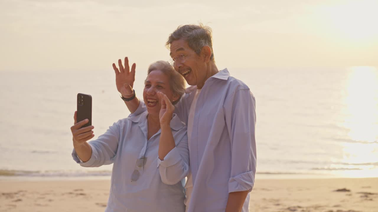 一对老年夫妇在日落时分用智能手机在海滩上视频通话。视频下载