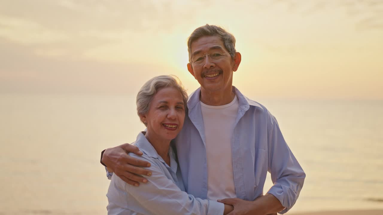 一对老年夫妇在日落时分在海滩上拥抱。视频下载