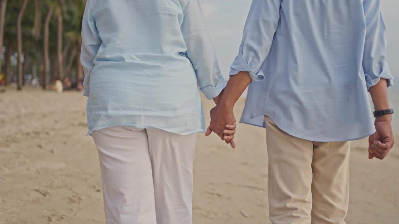 老人夫妇手牵着手在沙滩上散步。视频下载