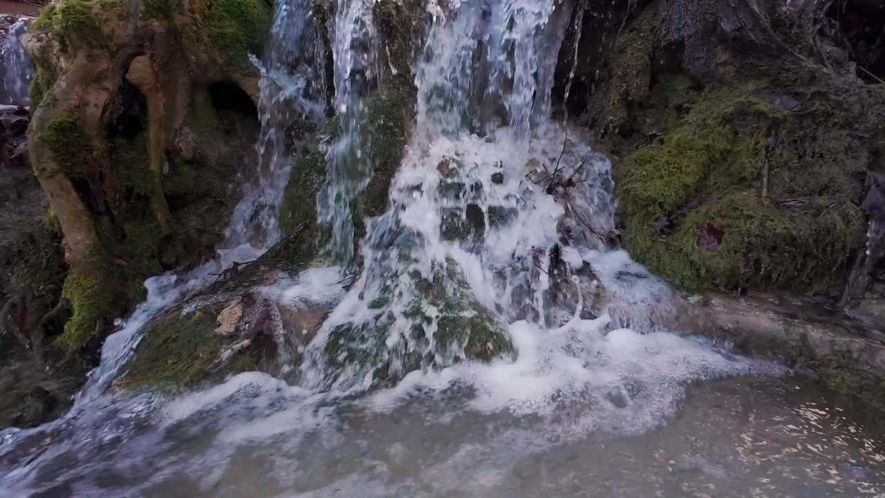 山间的一条小溪流，活灵活现，水花四溅。新鲜的泉水在长满苔藓和白雪覆盖的岩石间流淌。缓慢的运动。视频下载