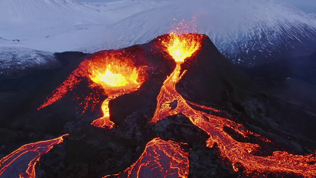 4K无人机拍摄的航拍电影镜头捕捉到了两个火山口喷出的熔岩，然后熔岩从下面倾泻而下，背景是白雪皑皑的冬季阿尔卑斯山。视频下载