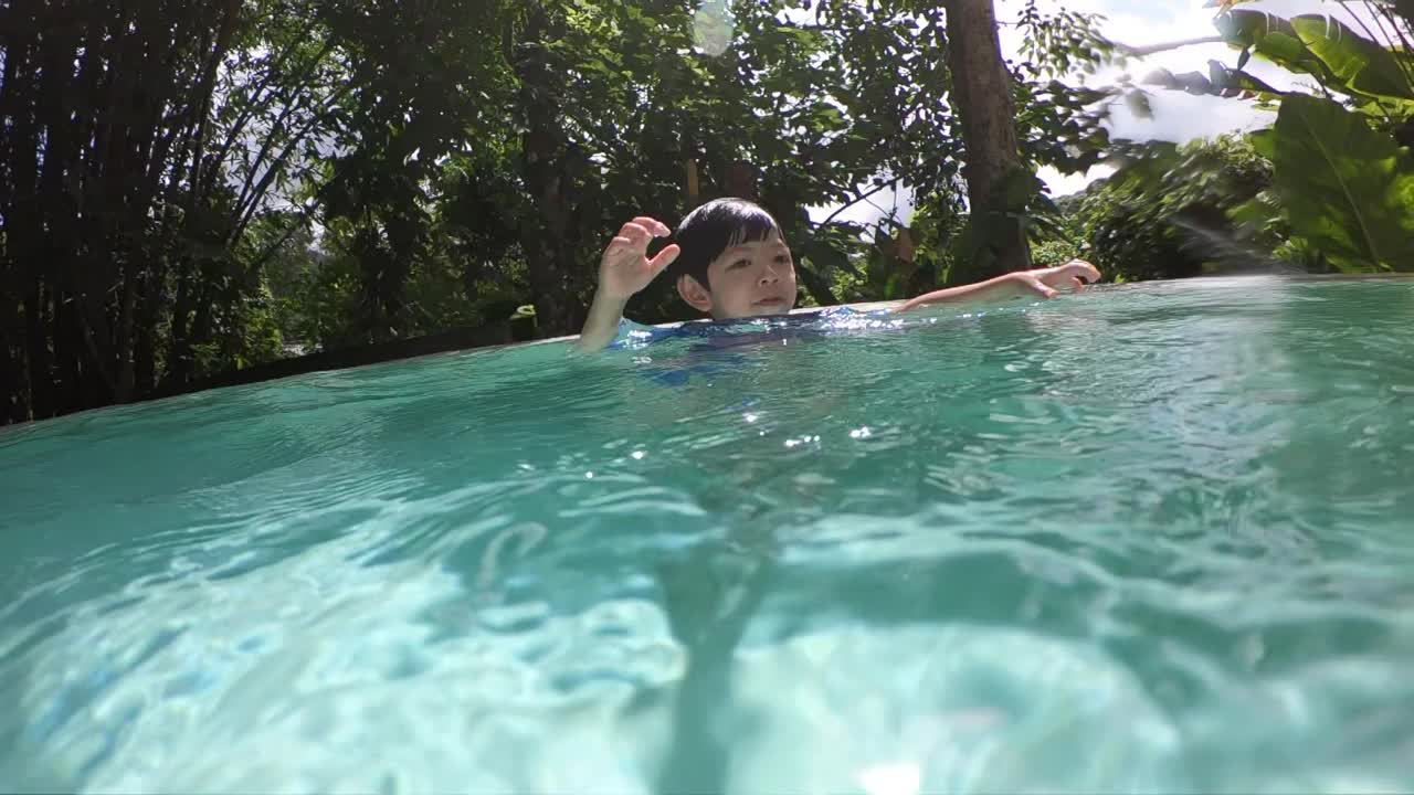 可爱的小男孩游进泳池，水面洒满阳光视频下载