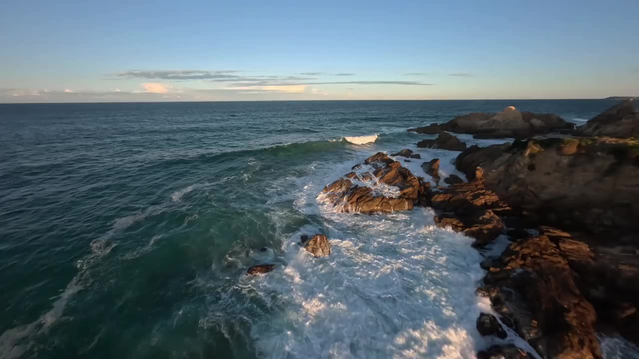 鸟瞰日落时海浪冲击岩石海岸线的景象。视频下载