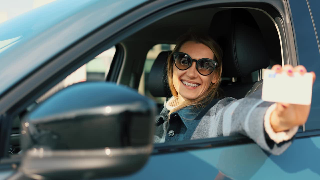 快乐的女人向车窗外展示她的新驾照，然后开车走了视频下载