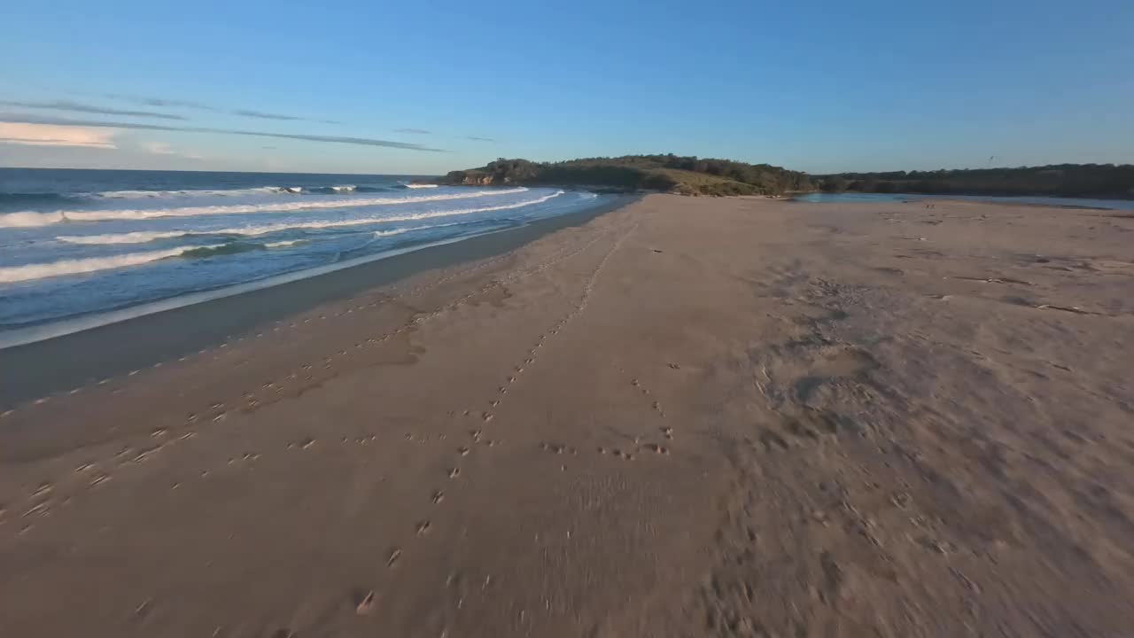鸟瞰图沿着沙滩上的脚印低空飞行，然后经过两个人。视频下载