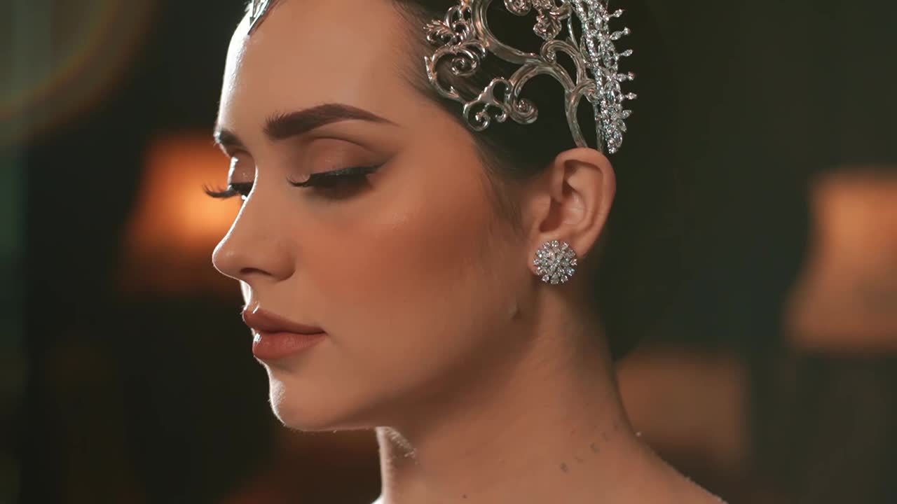 优雅的女人，带着复古的妆容和发型，戴着皇冠和耳环，背景是柔和的灯光。视频下载
