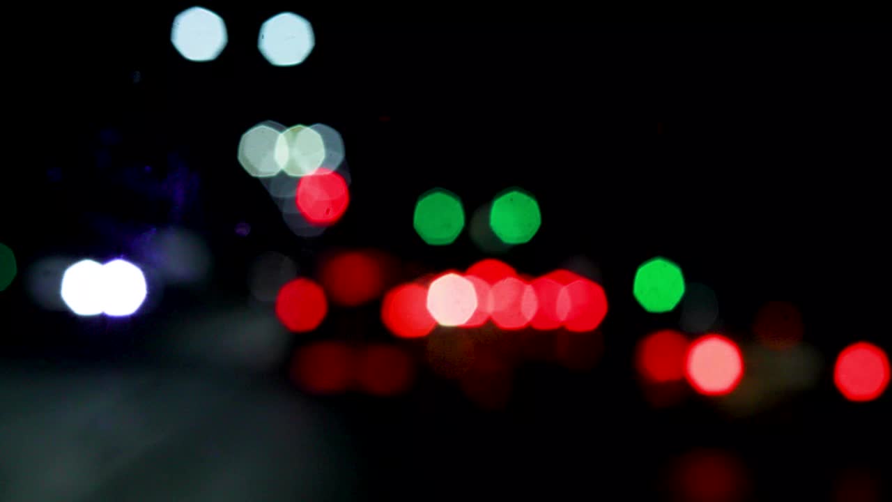 迷离的多色红灯笼和汽车前灯透过挡风玻璃在雨中，在黑暗中视频下载