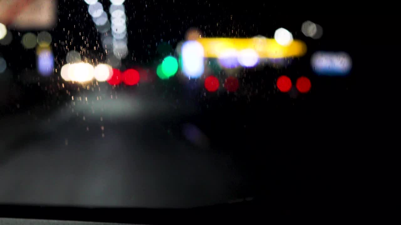 模糊的红绿黄灯和汽车前灯透过挡风玻璃在雨中潮湿的道路上，在黑暗中视频下载