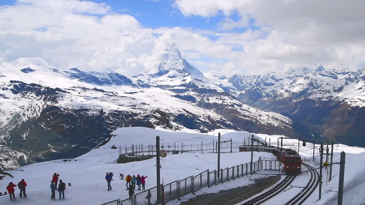 瑞士马特洪峰火车站，白雪覆盖的铁路上的红色火车与游客们在一起视频下载