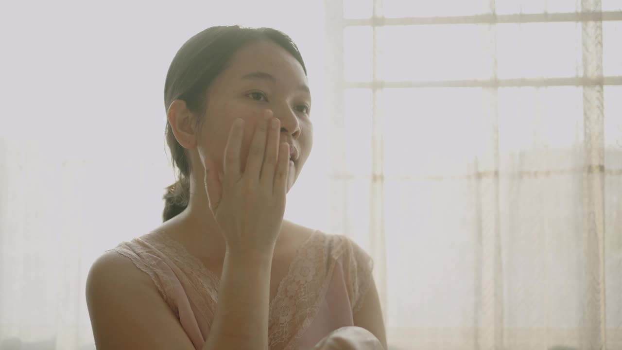 亚洲女性用一只手在脸颊和颈部涂抹润肤霜。视频下载
