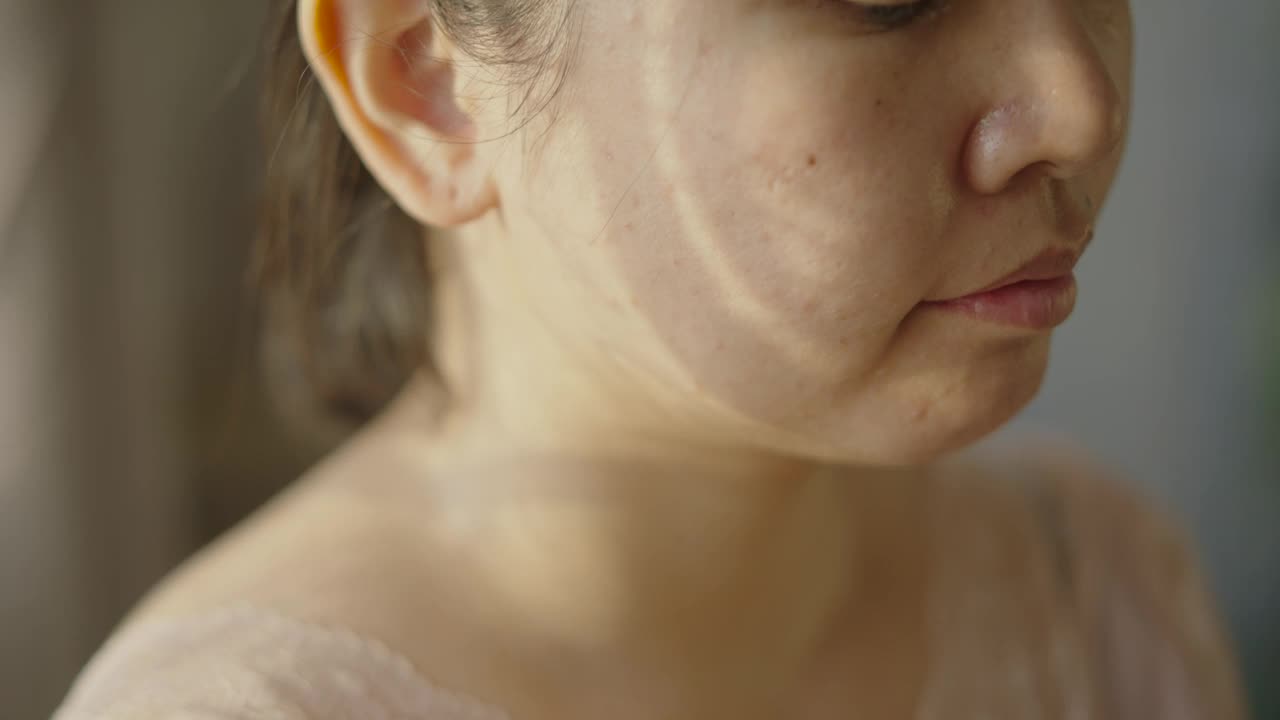 亚洲女性用一只手在脸颊上涂抹润肤霜。视频下载