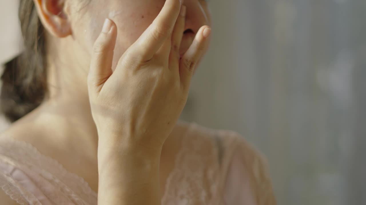 快乐的亚洲女性用一只手在脸上和脖子上涂抹润肤霜。视频下载