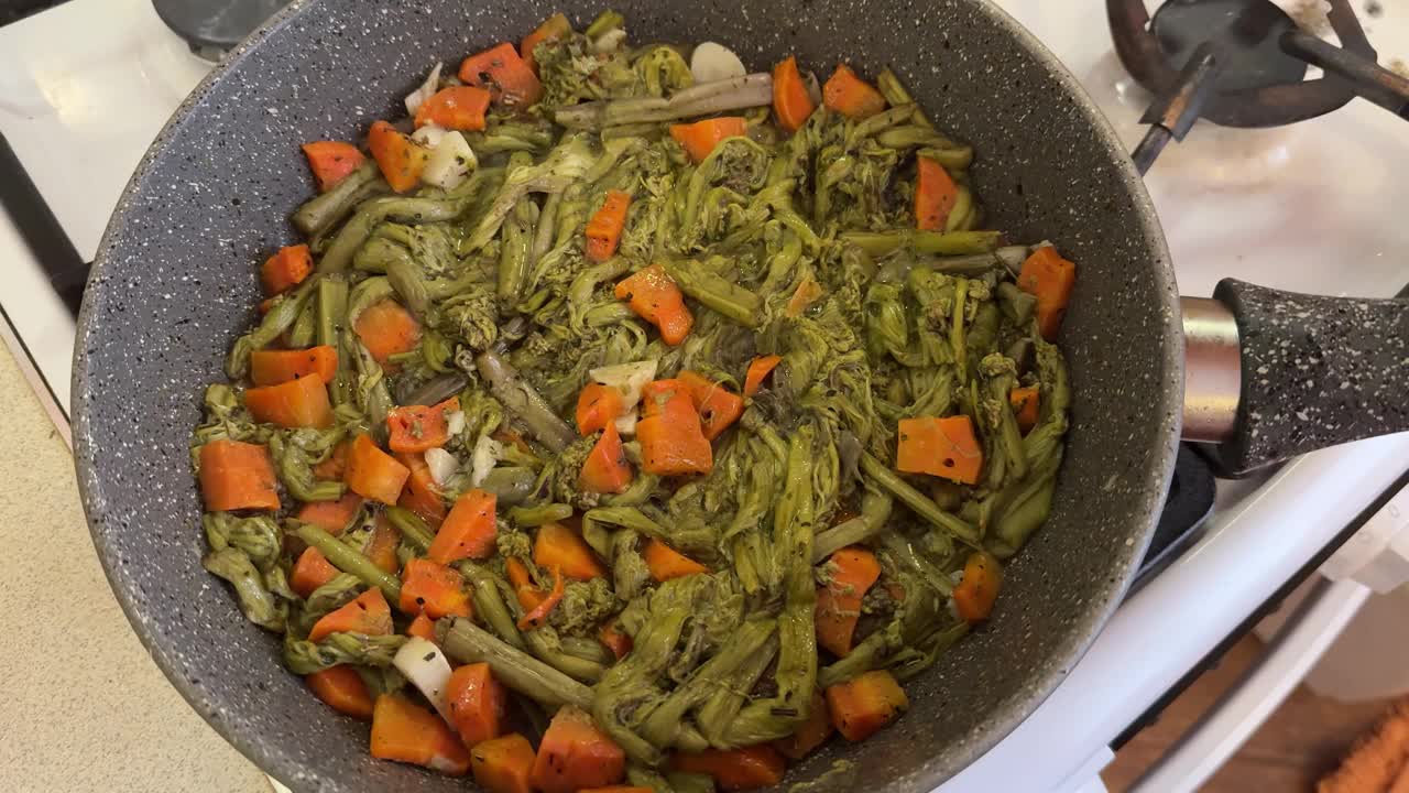 在煤气炉上用煎锅，用洋葱和胡萝卜烤蕨菜。健康饮食。近距离视频下载