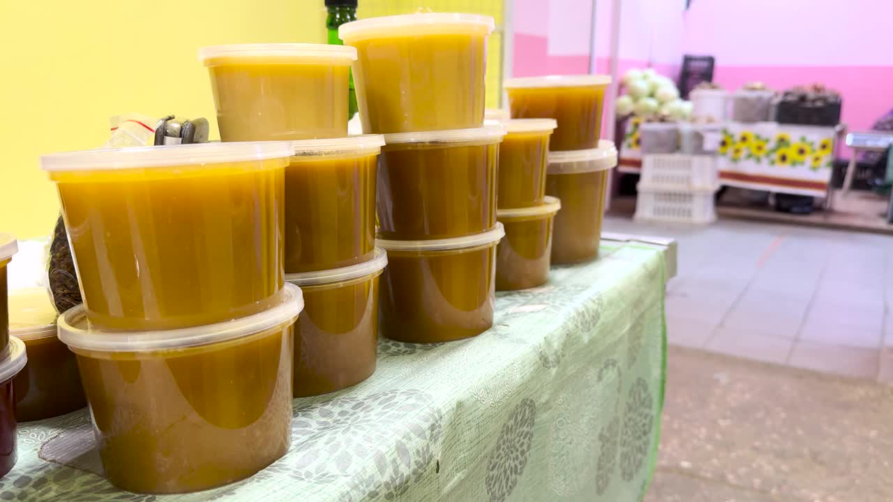 农贸市场上堆放着装满蜂蜜的塑料容器。有许多装着各种类型和颜色的天然甜蜂蜜的罐子在出售视频下载