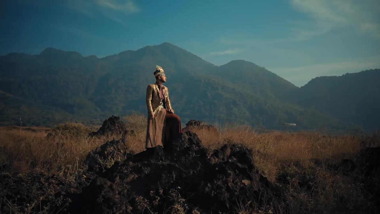 一个穿着复古服装的男人站在田野里，背景是群山。视频下载