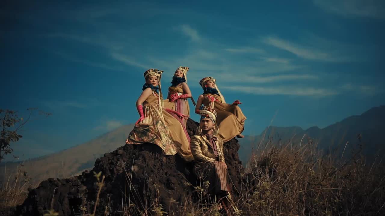 四个女人穿着飘逸的裙子，头戴皇冠，坐在一块露出地面的岩石上，背景是群山视频下载