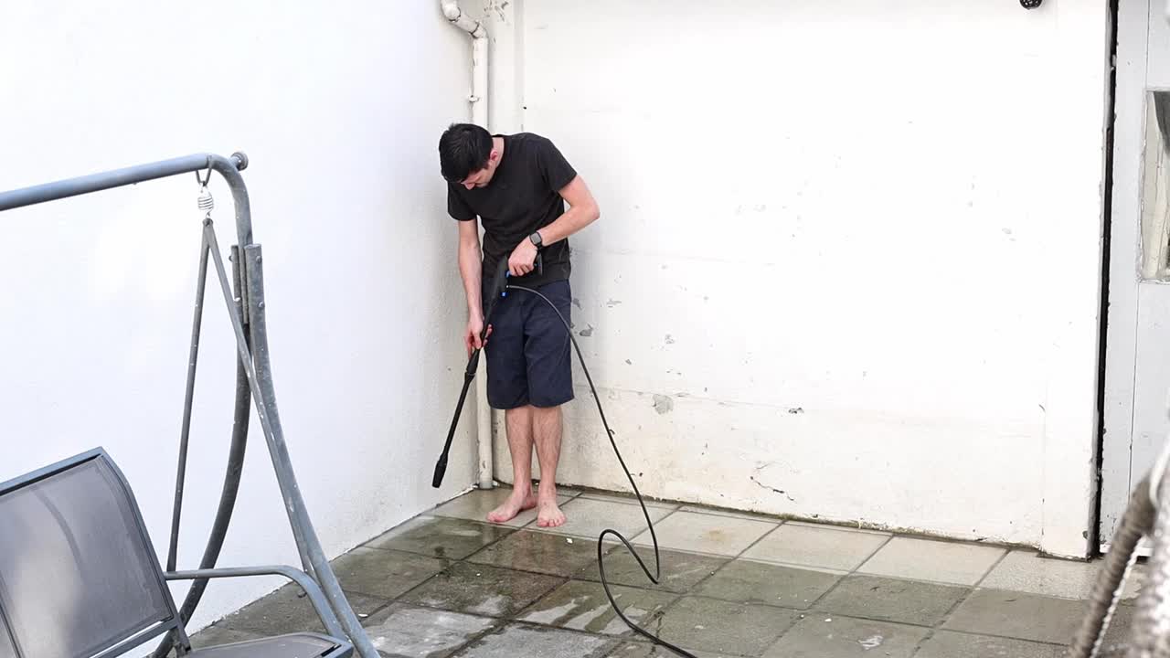 一个年轻人在后院用Karcher洗花园瓷砖。视频下载