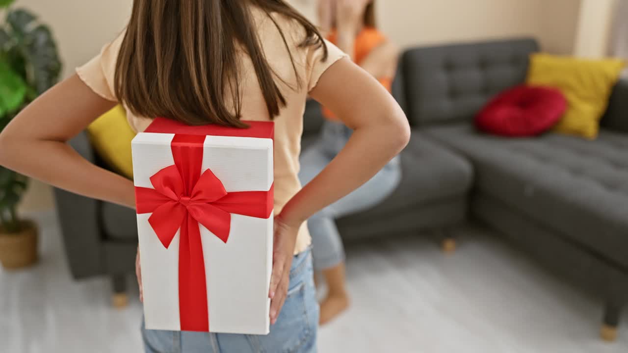 在舒适的客厅里，女人送礼物给女孩一个惊喜，表达爱意、亲情和庆祝。视频下载