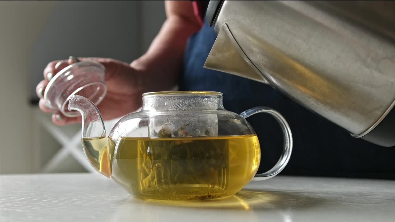 女孩在厨房用绿茶把热水从水壶倒进茶壶视频下载