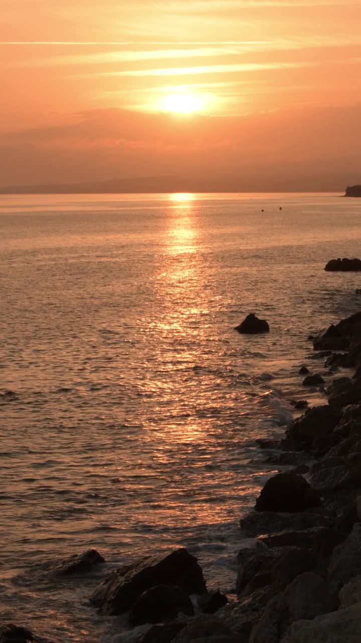 在岩石海滩上日落。4 k垂直视频下载