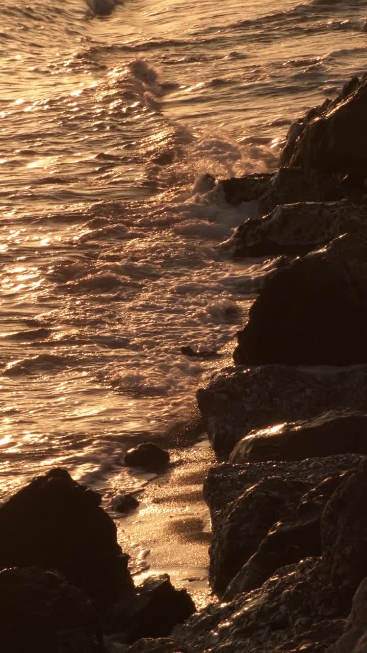 日落时在岩石海滩上的金色波浪。4 k垂直视频素材