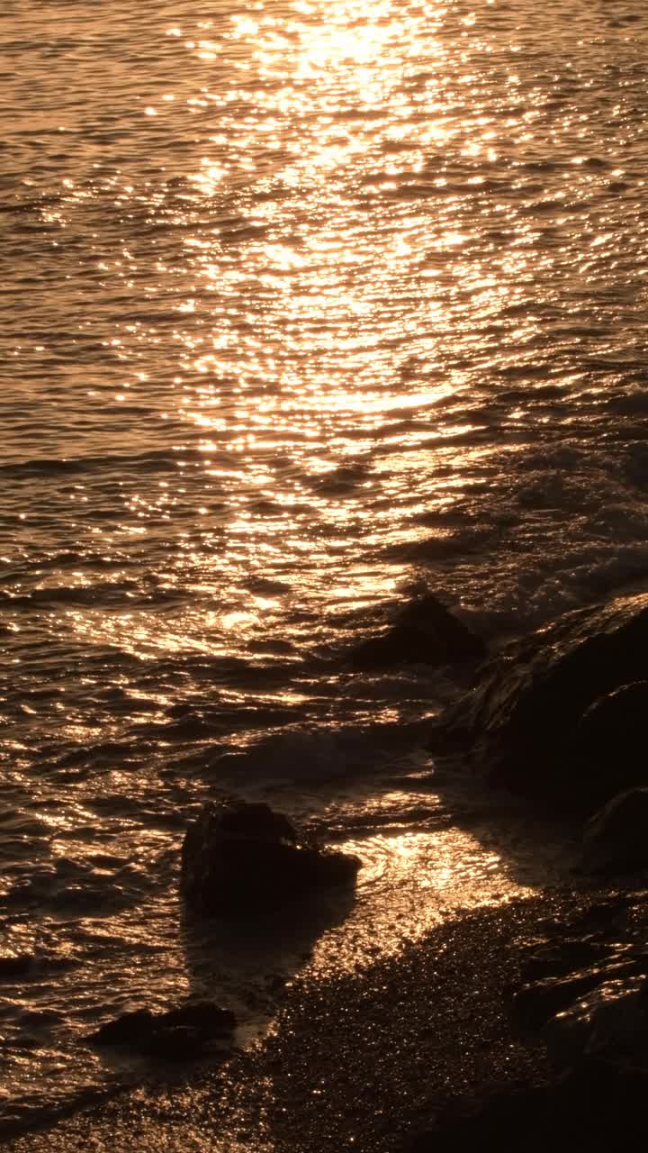 日落时在岩石海滩上的金色波浪。4 k垂直视频下载