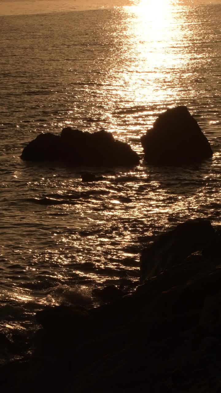 日落时岩石海滩上的岩石。4 k垂直视频下载