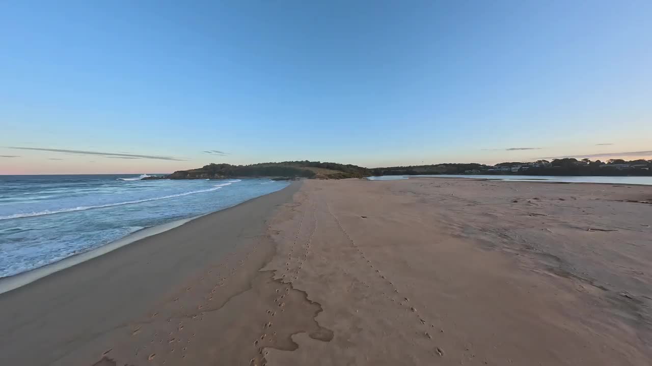 鸟瞰图低空飞过沙滩上的脚印，然后经过两个人，飞行员和另一个正在拍摄日落。视频下载