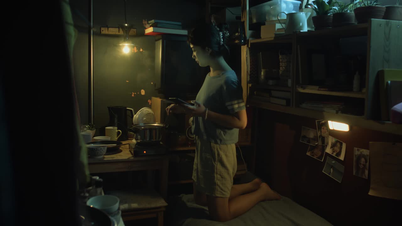 中国女孩用智能手机在黑暗的鞋盒公寓里做饭视频下载