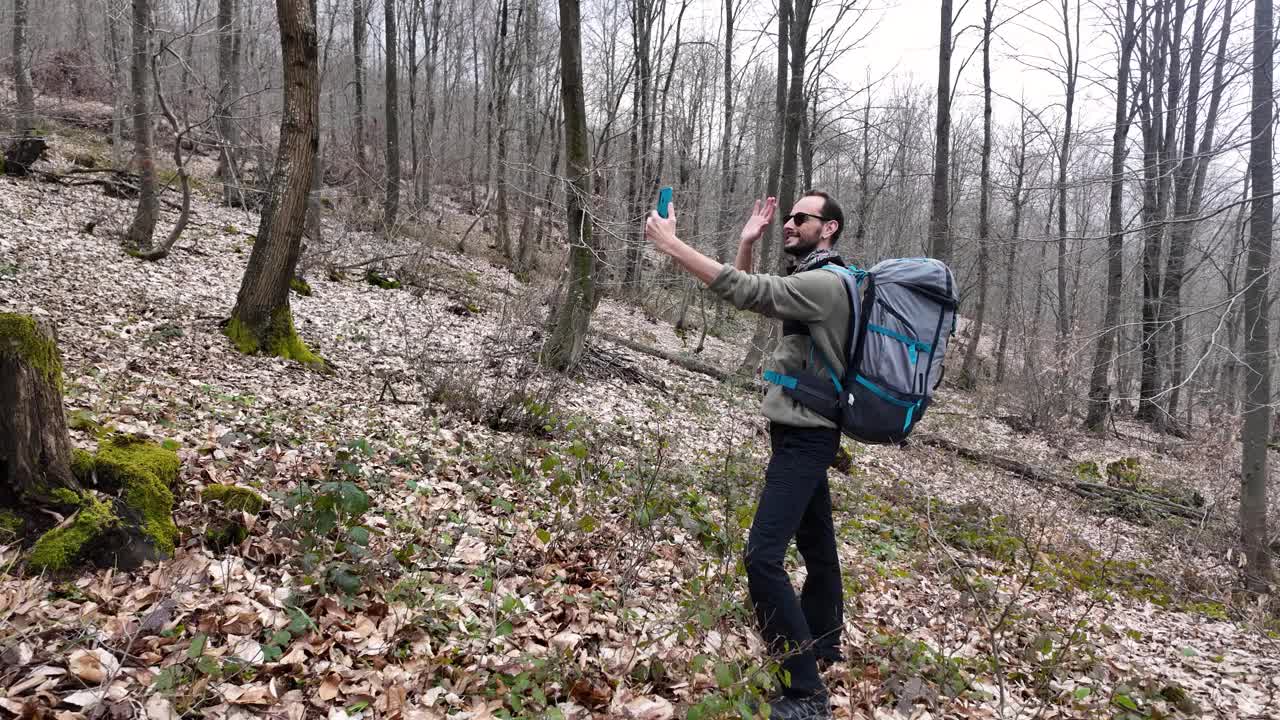 独自徒步旅行的男性在森林里自拍，背着背包打视频电话。视频下载