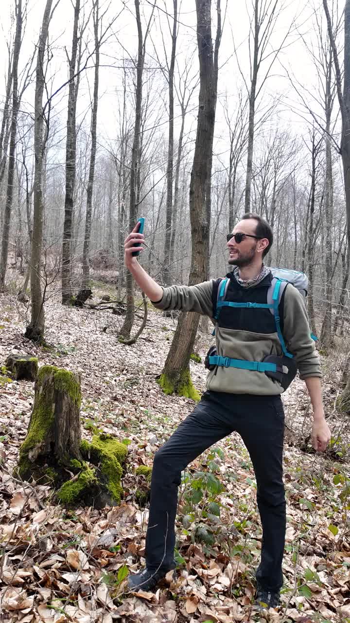 独自徒步旅行的男性在森林里自拍，背着背包打视频电话。垂直的。视频下载