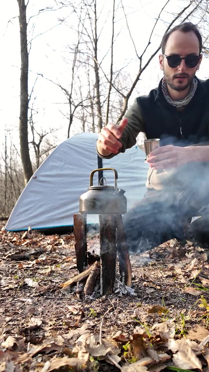独自露营者在森林里往杯子里倒酒，喝玫瑰果。野营帐篷。篝火。视频下载