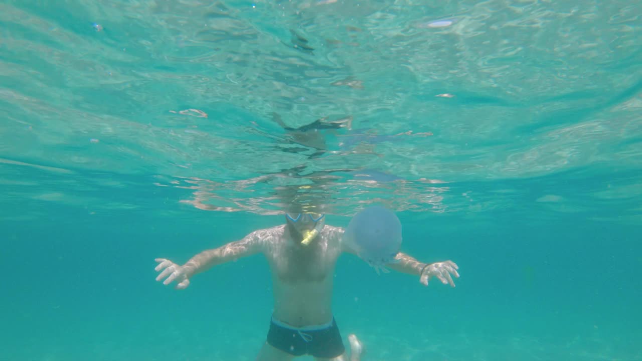 戴着面罩，戴着通气管的大胡子男子在水下浅水区自由潜水。在阳光明媚的日子里浮潜。视频下载