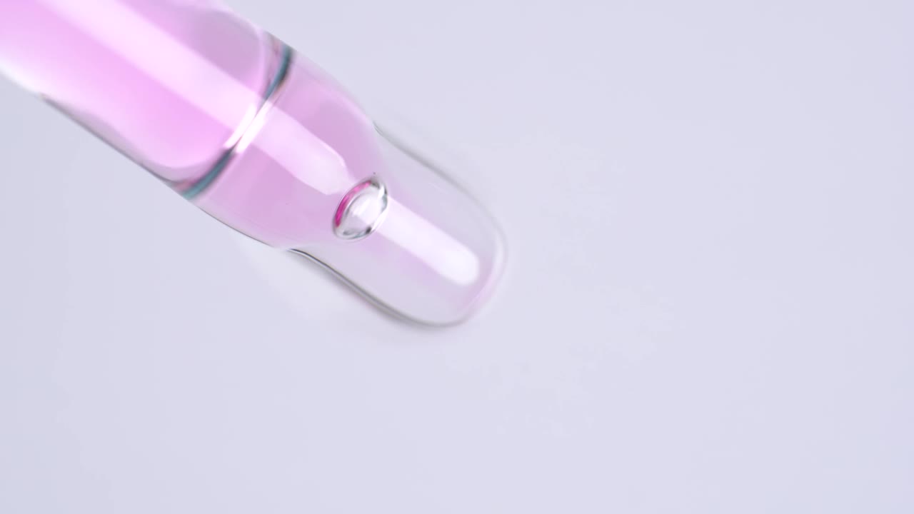 微距拍摄粉红色的油血清流从滴管在白色背景。用于身体、面部或指甲的护肤化妆品。化妆品血清中分子气泡的运动视频下载
