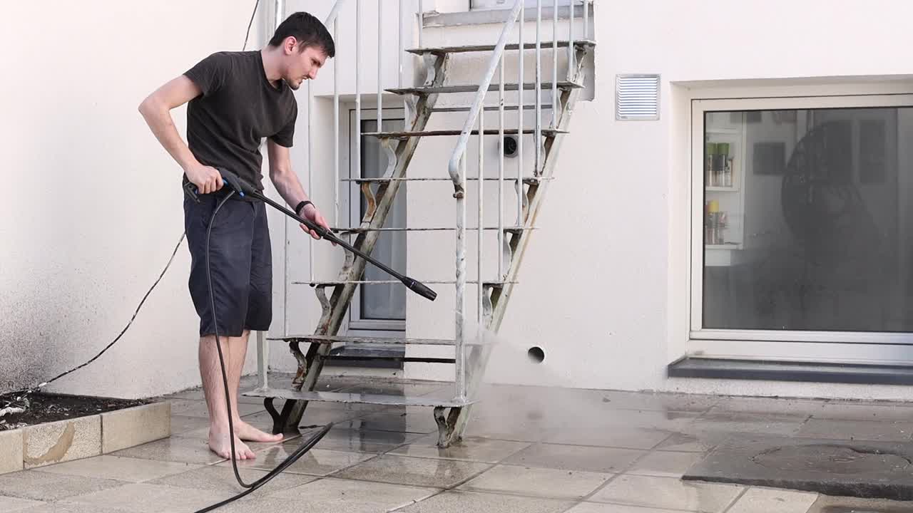 一个年轻人正在用Karcher洗院子里花园楼梯的栏杆。视频下载