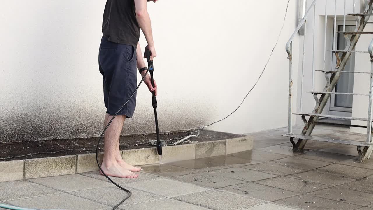 一个年轻人用Karcher洗花园瓷砖。视频下载