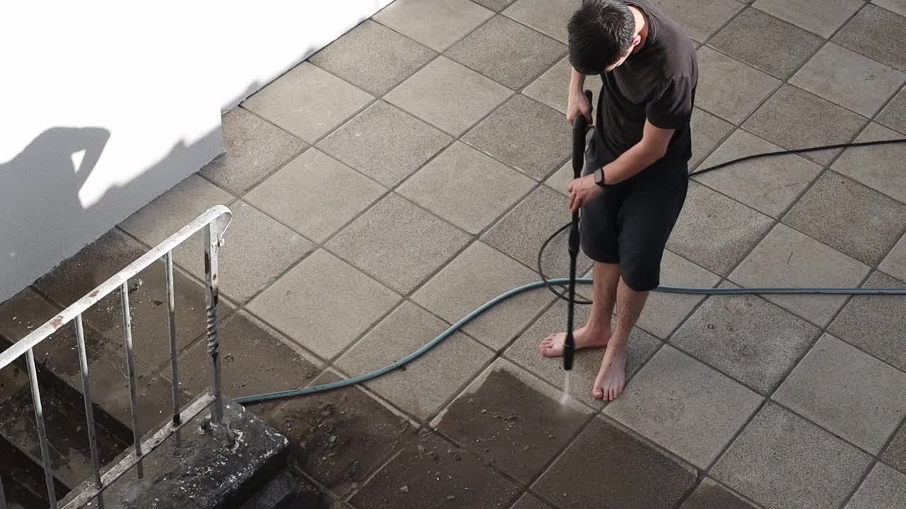一个年轻人在他的院子里用Karcher洗花园瓷砖。视频下载