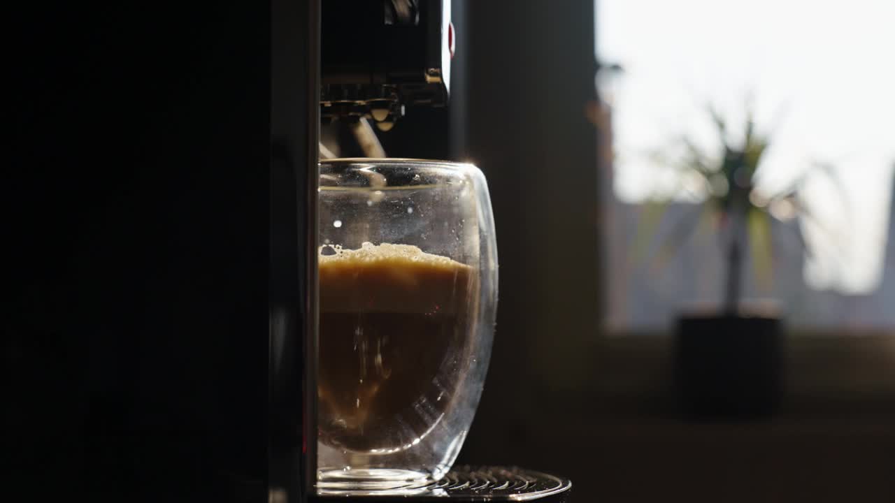 自动咖啡机准备卡布奇诺在玻璃杯与早晨的阳光，男性手拿一杯咖啡。每天早晨例行公事视频下载