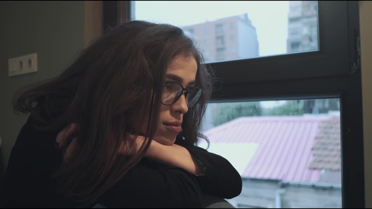 沉思的年轻女子凝视着下雨的窗外，沉浸在孤独和沉思中视频下载