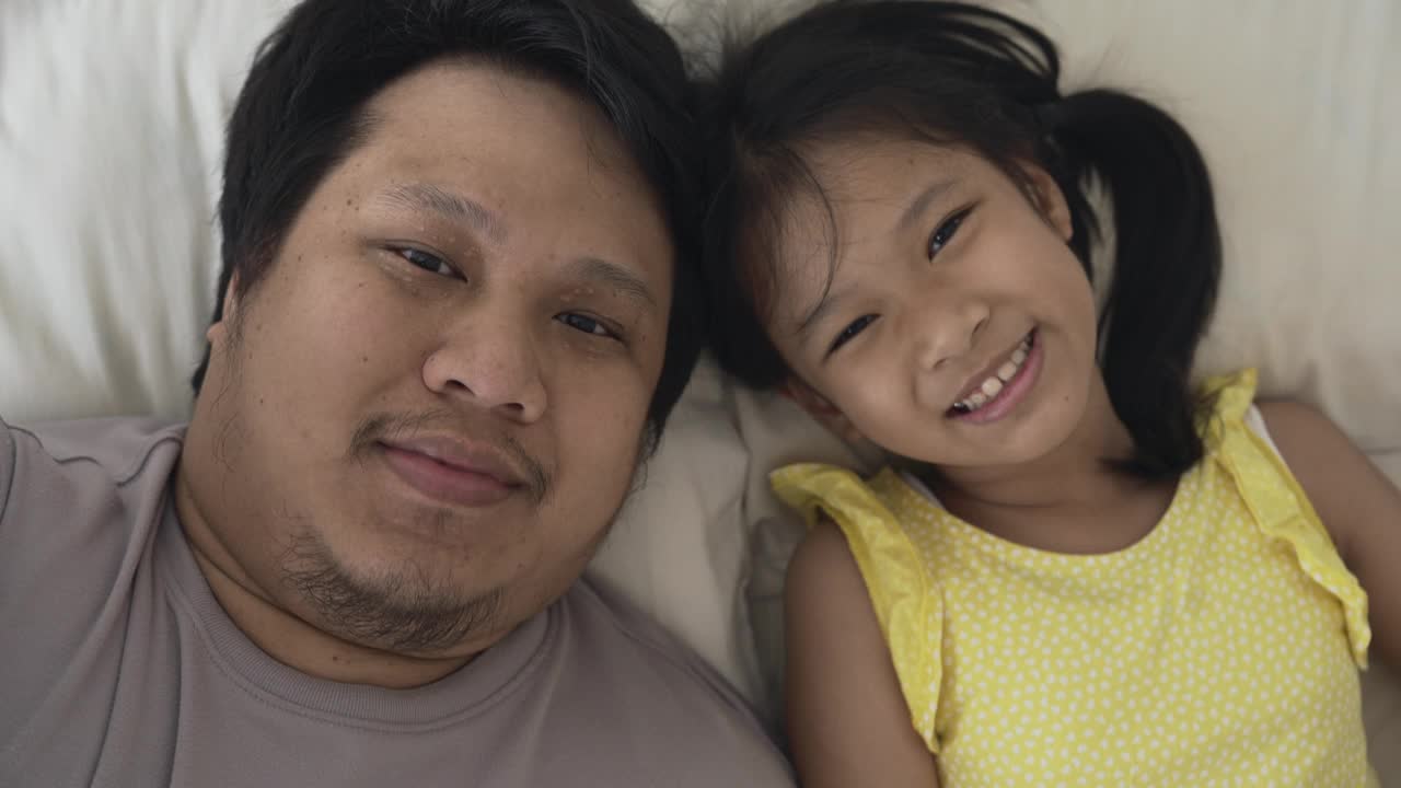 快乐的父亲和女儿看着相机，在床上自拍视频视频下载