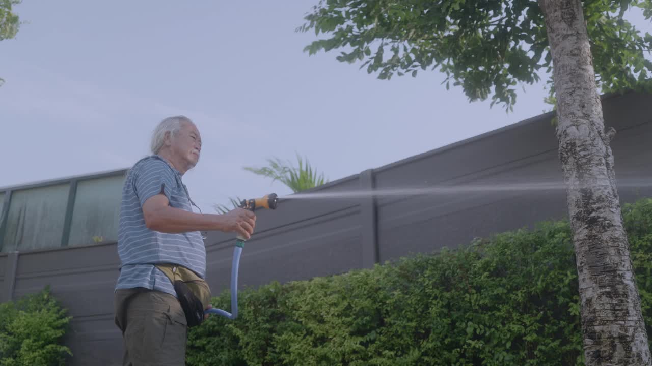 一位亚洲祖父带着孙子和妻子在家里用水管给植物浇水。视频下载