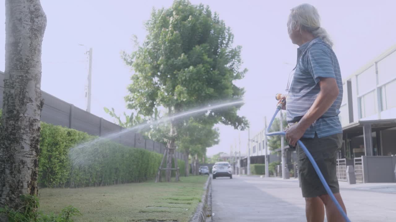 一位亚洲祖父带着孙子和妻子在家里用水管给植物浇水。视频下载