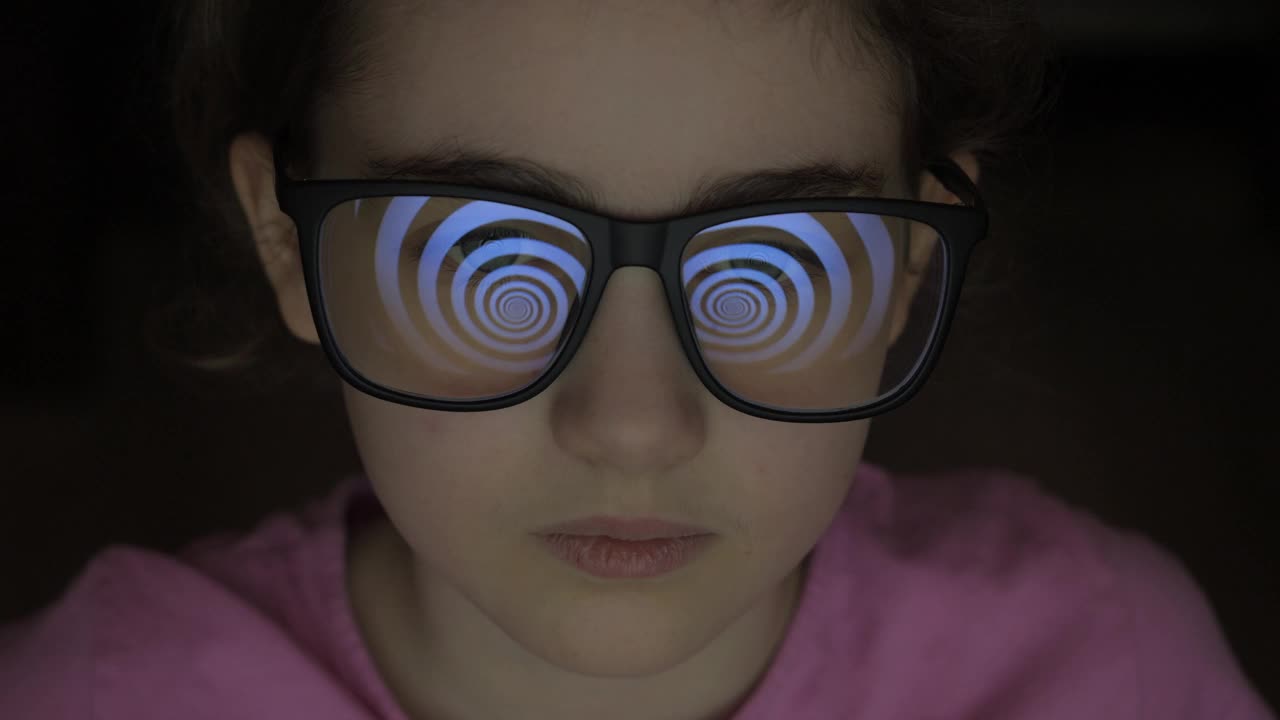 戴眼镜的小女孩看着催眠屏幕。媒体对人的影响。传播虚假信息，恶作剧，宣传洗脑虚假信息。操纵群众伪造，虚假信息。视频下载
